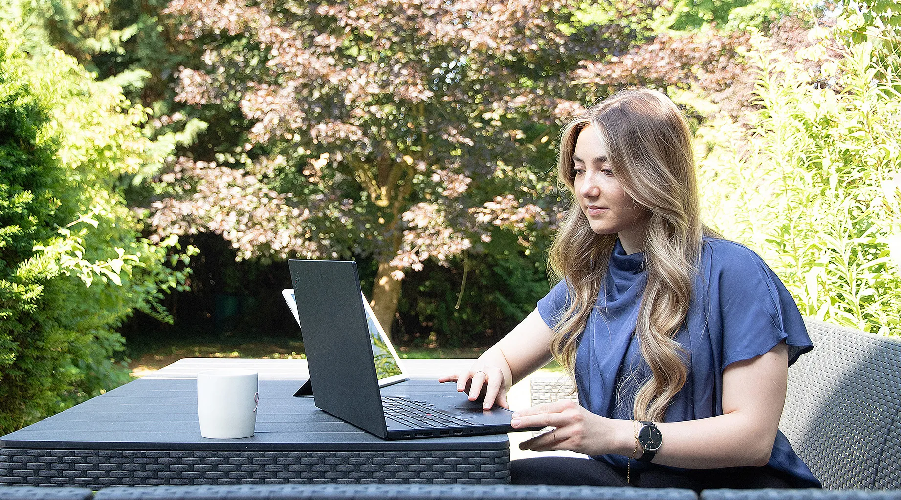 Dieselbe Mitarbeiterin arbeitet am Laptop im Home-Office im Garten